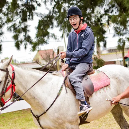 Un joven sonriente monta a caballo durante su sesión de equinoterapia