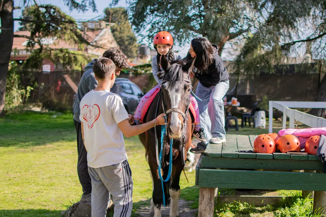 Una paciente a caballo al comenzar su sesión, con el asistente ecuestre sosteniendo al caballo del cabestro