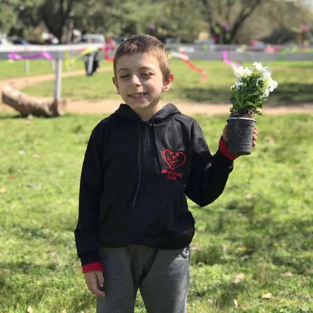 Un paciente sonríe sosteniendo una planta con flores, en el predio de Alaia