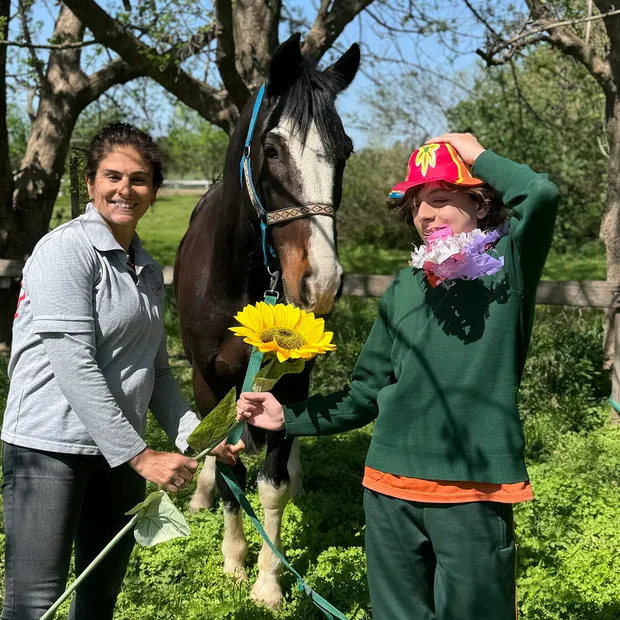 Una profesional y un paciente junto a uno de los caballos, con una flor en la mano